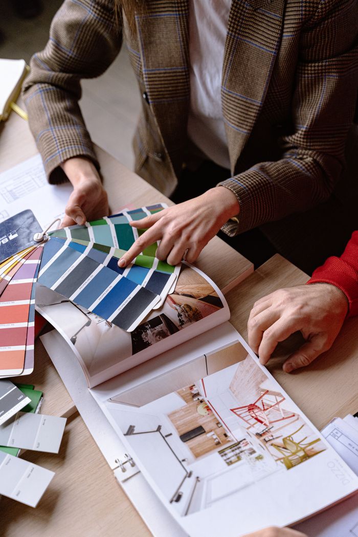 ours-journey Interior designers discuss color swatches and design ideas at a table, planning a creative project.